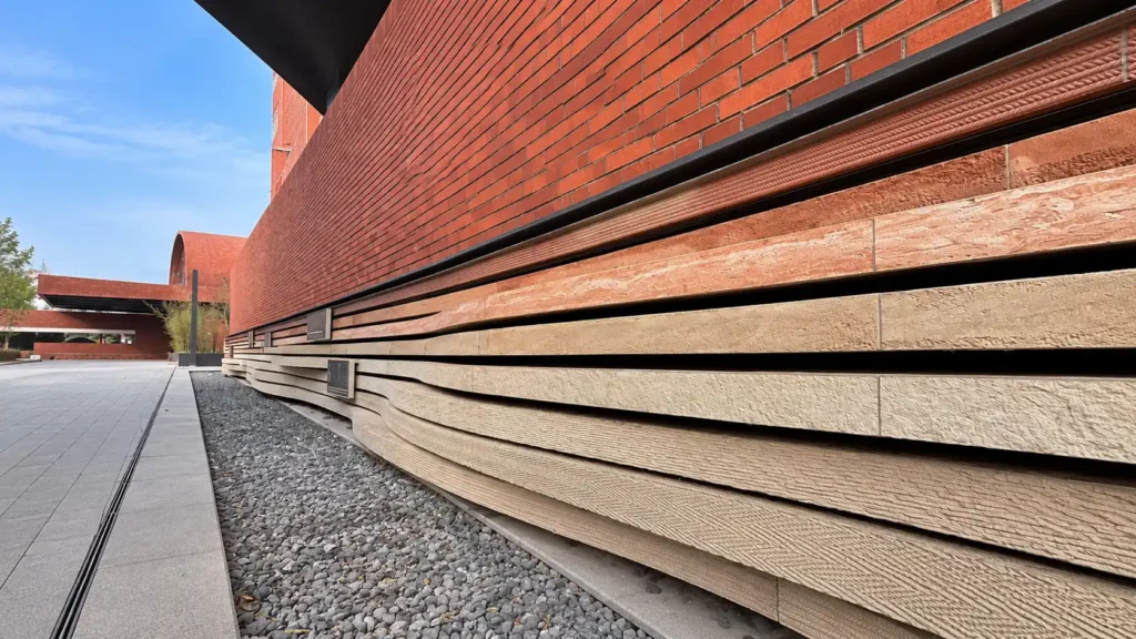 Curved layered stone cladding along a red brick building exterior