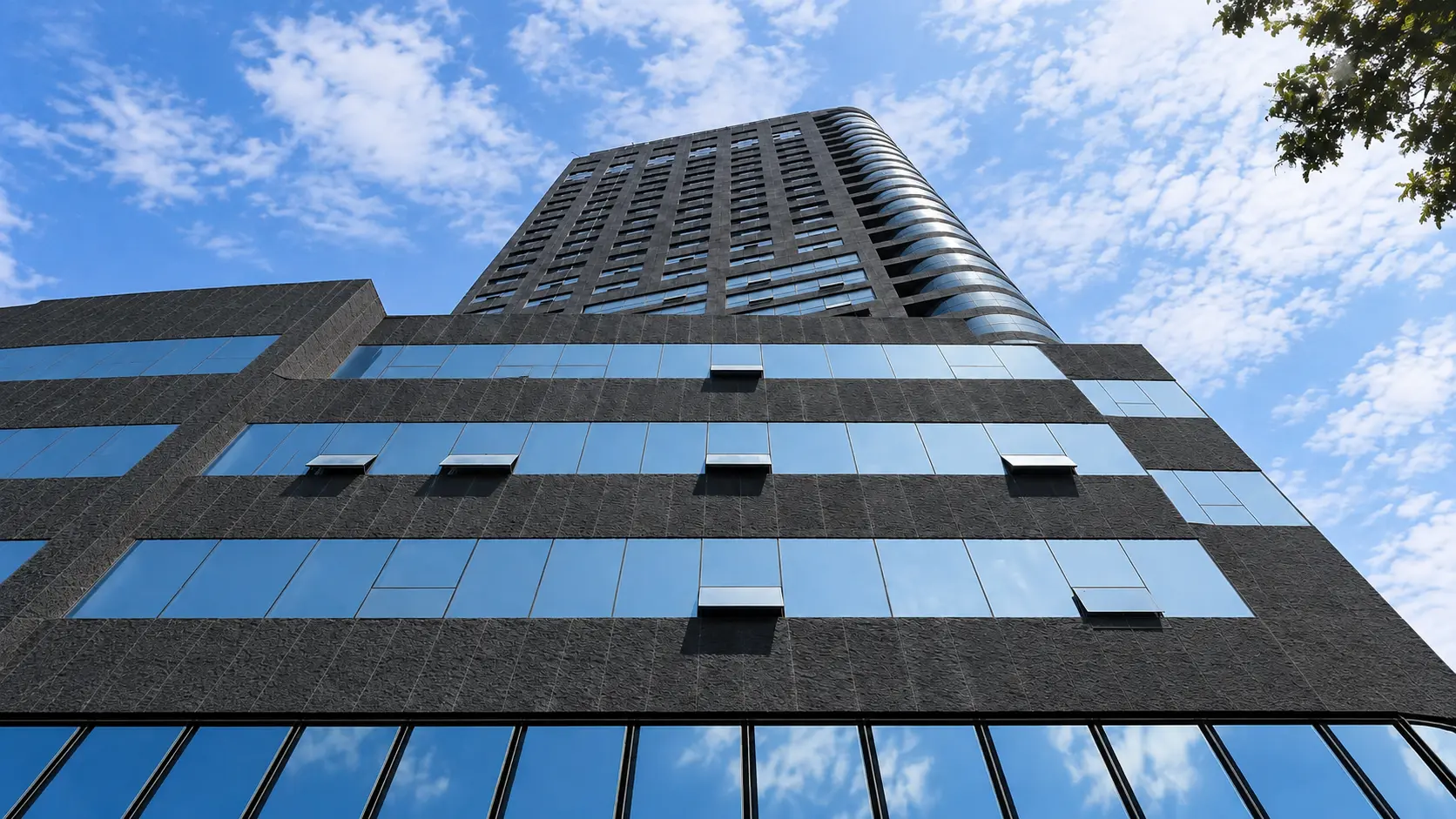 Dark textured exterior cladding on a modern high-rise building with reflective glass windows