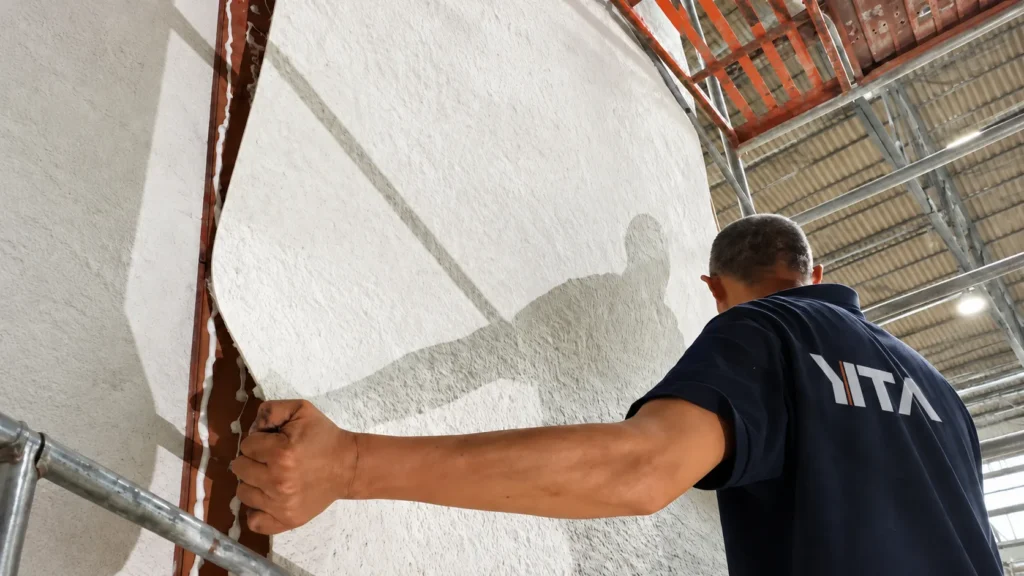 Worker installing a large light beige flexible stone veneer on an interior wall
