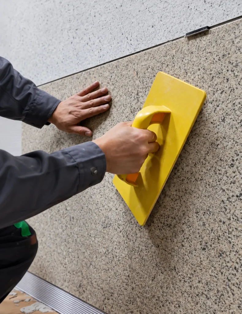 Worker pressing a flexible stone sheet firmly against the wall to ensure full adhesive contact and avoid hollow areas.