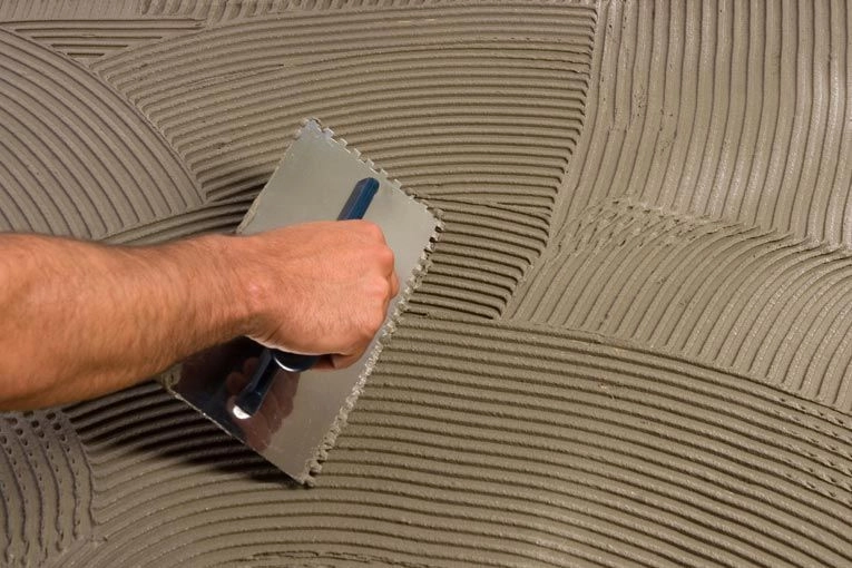 Applying C2S1 cement-based flexible adhesive mortar with a notched trowel for MCM flexible stone installation.
