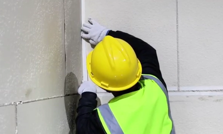 Installer applying masking tape along a flexible stone internal corner before joint sealing.